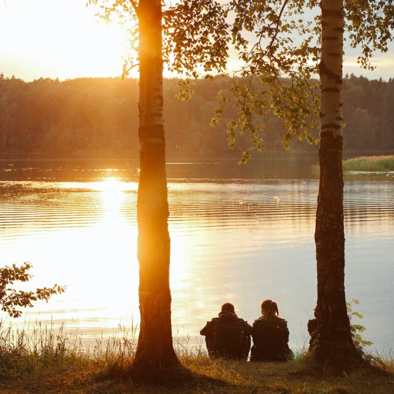 man and woman sitting near body of water during sunset